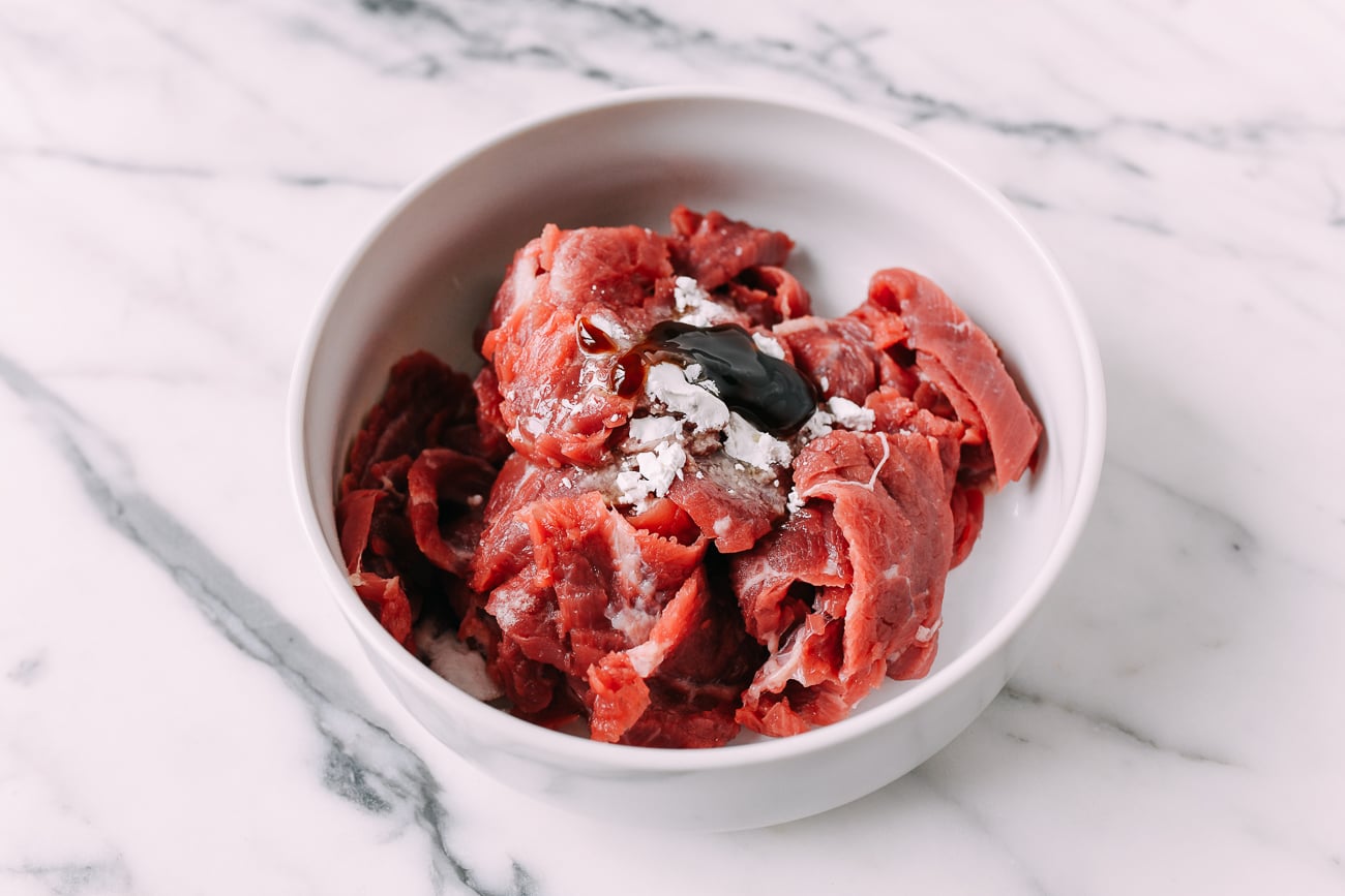 Sliced flank steak with marinade ingredients in white bowl