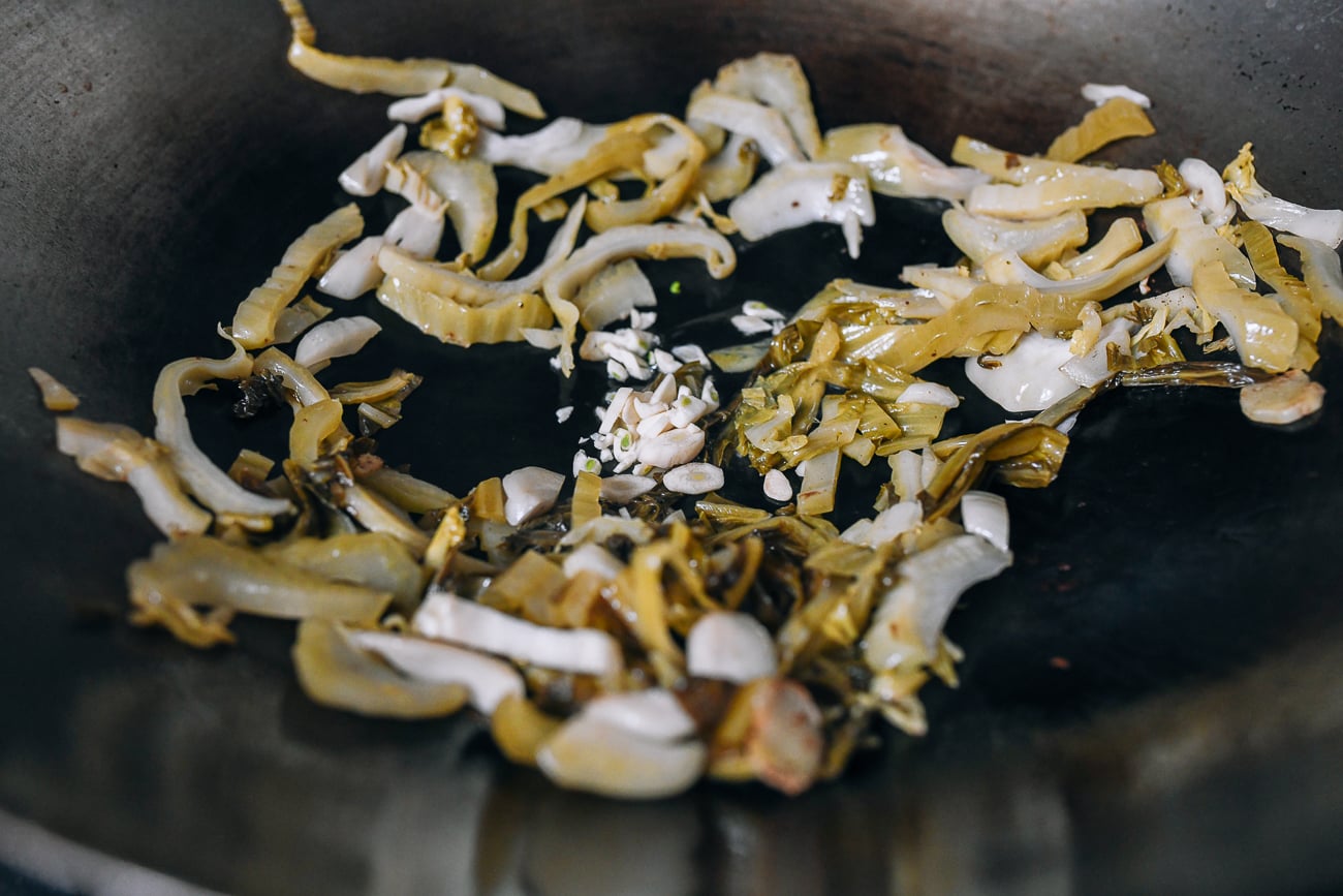 Adding garlic to pickled mustard greens in wok