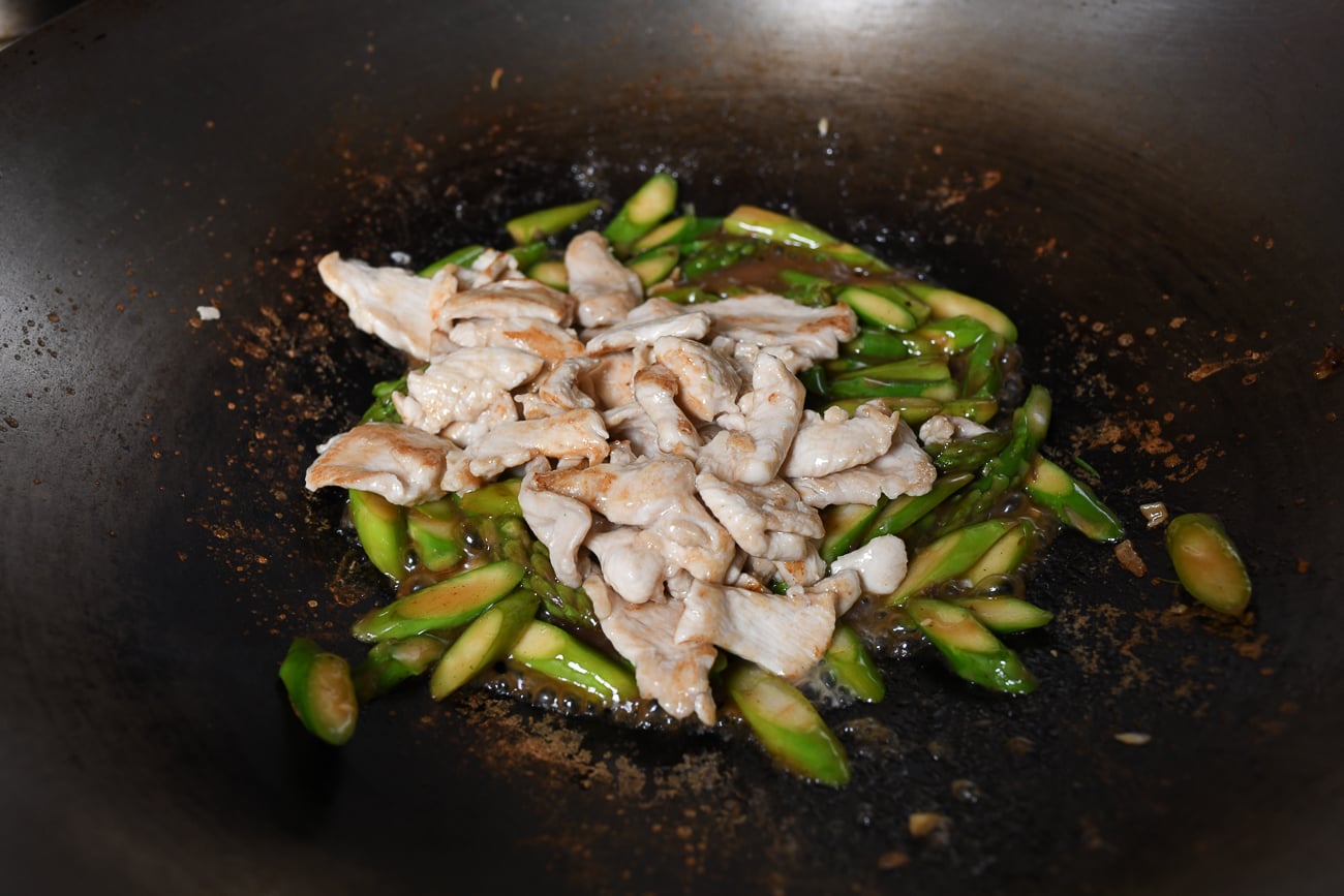 Adding chicken to asparagus in wok