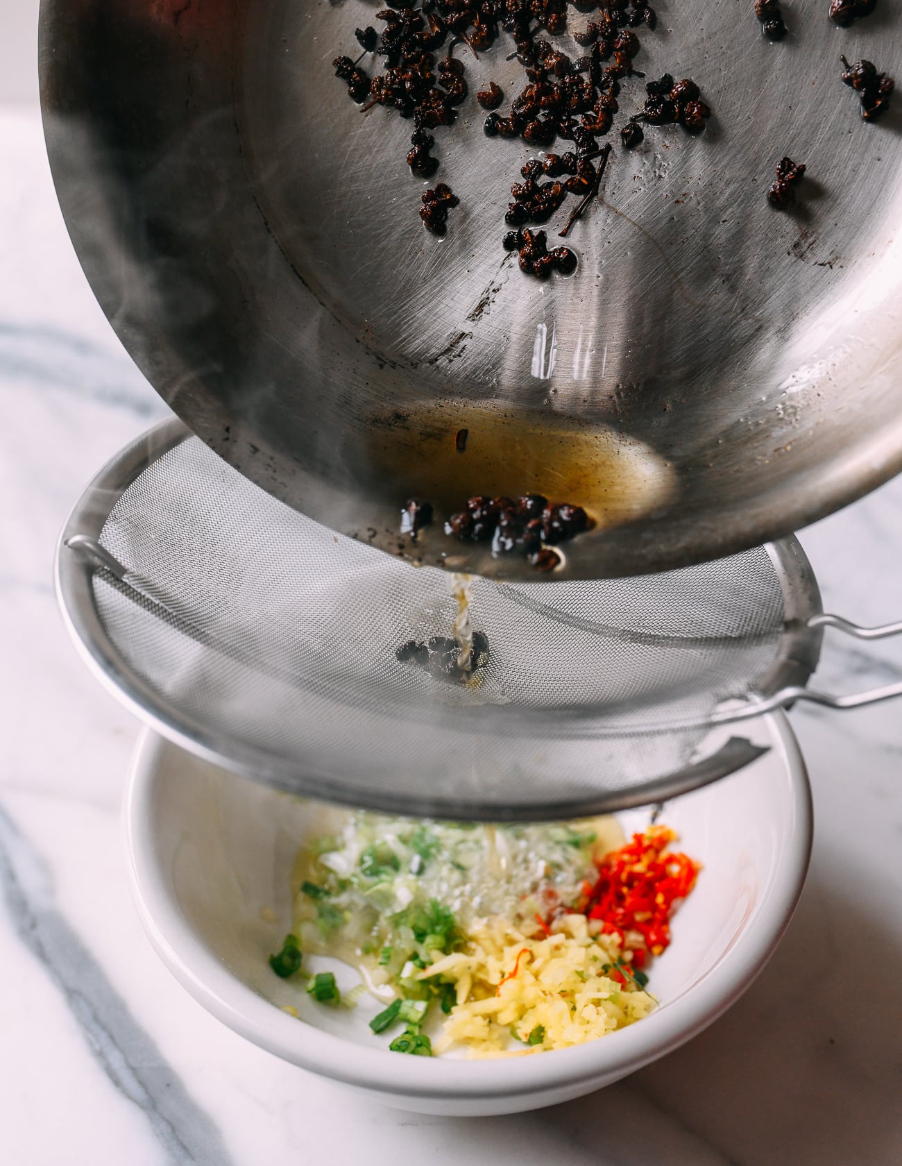 Pouring oil through fine meshed strainer into aromatics