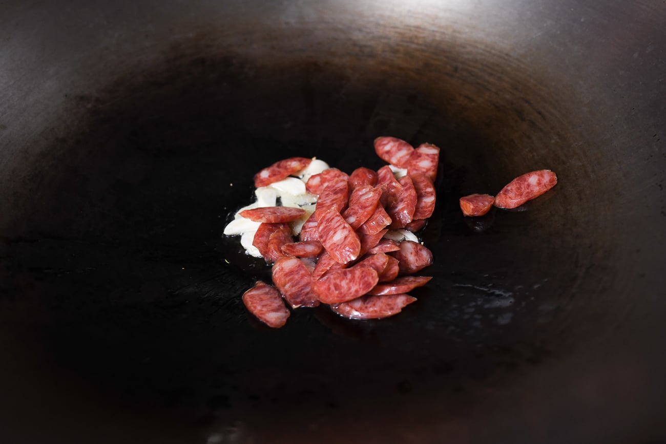 Adding Chinese sausage slices to wok