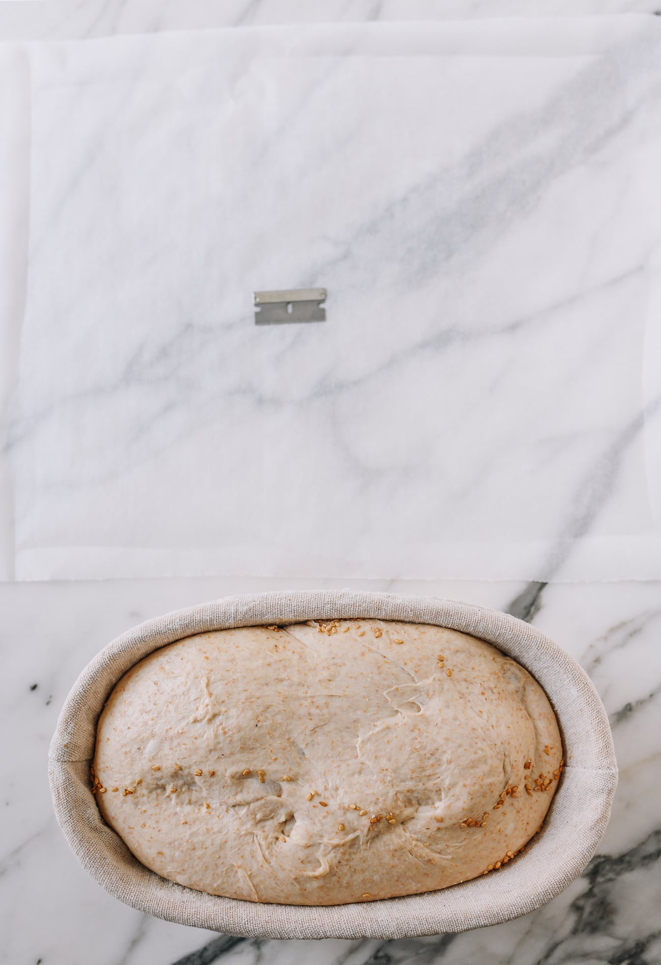 Cold fermented dough next to parchment paper and razorblade for slashing
