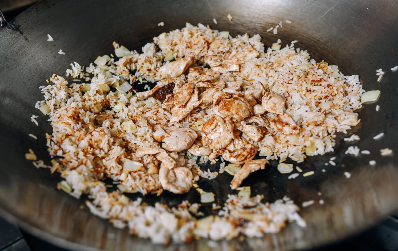 Adding cooked chicken to rice in wok