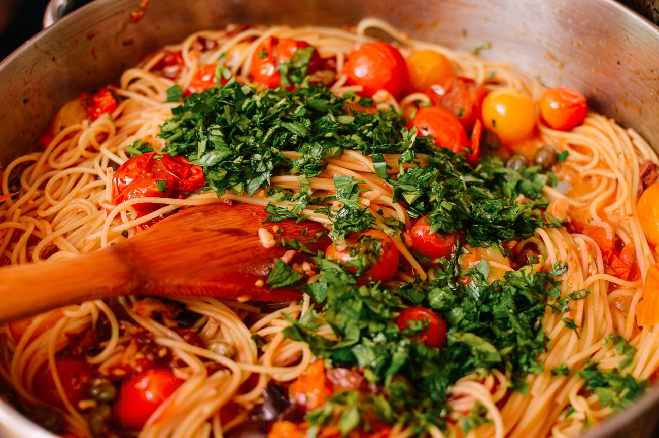 Tossing together spaghetti with roasted tomatoes and chopped parsley