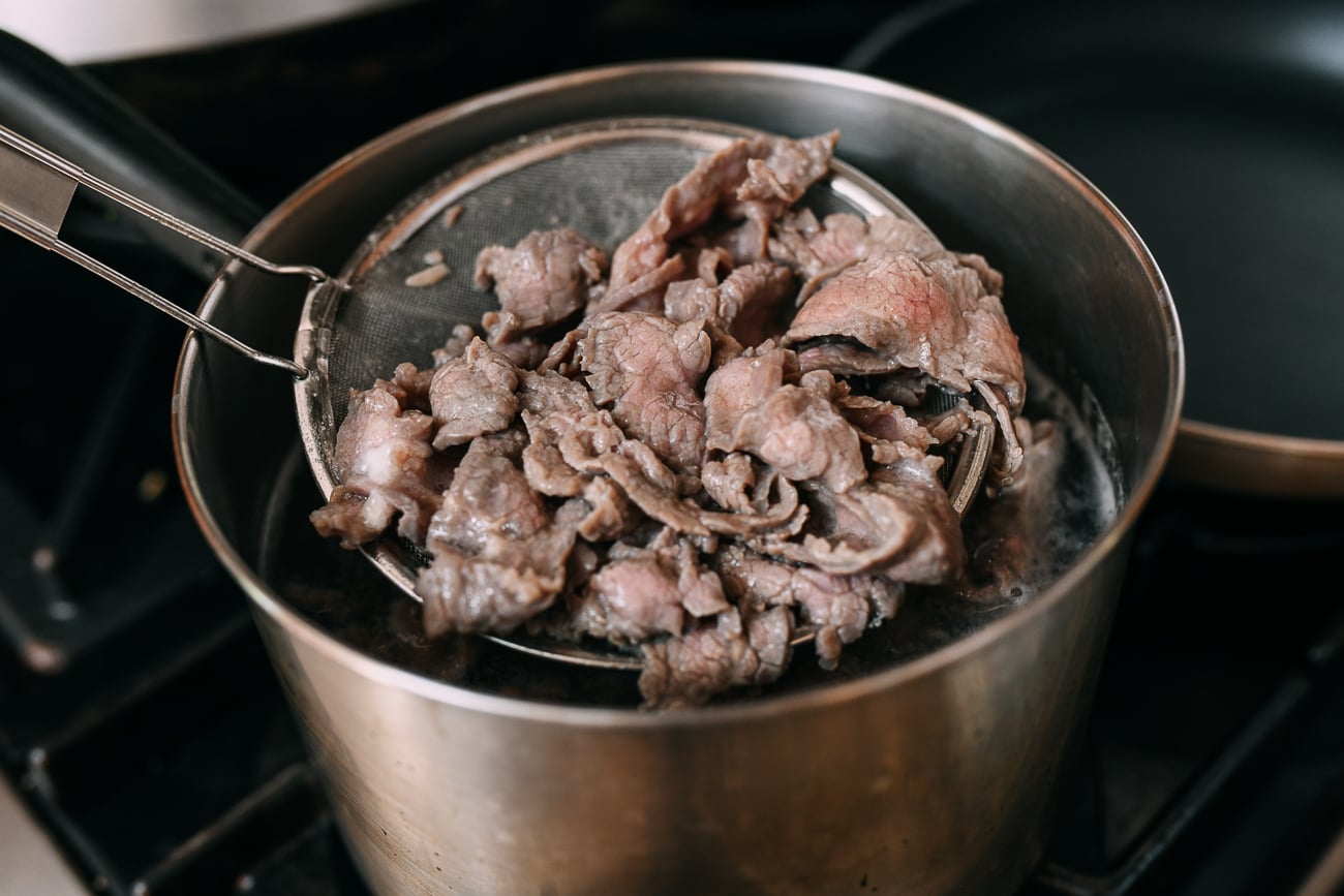 Removing blanched beef slices from pot with strainer