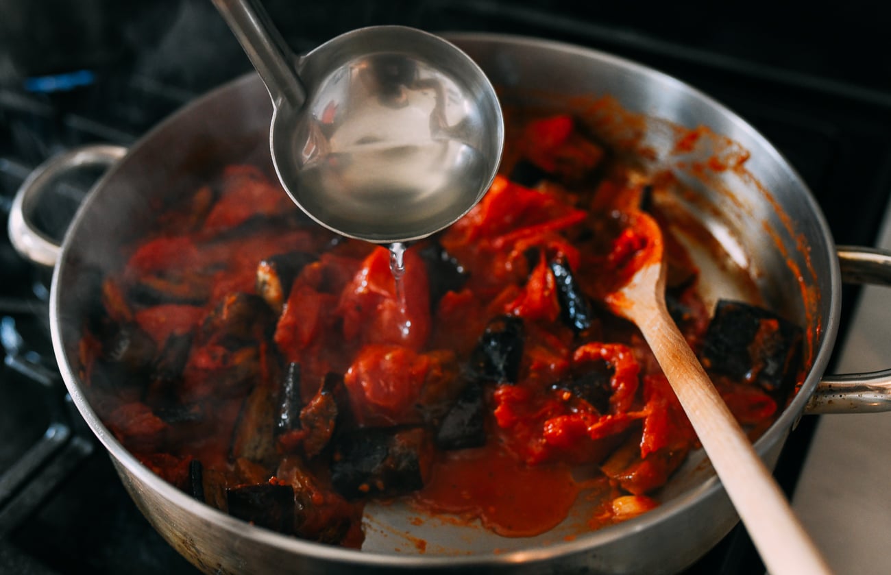 Adding pasta water to pan of tomatoes and eggplant