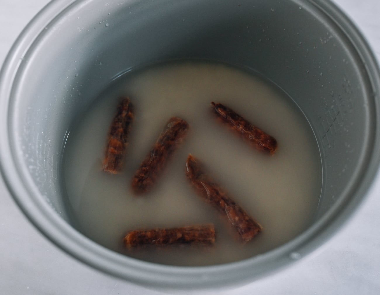 Lap Cheong on top of rice and water in rice cooker pot.
