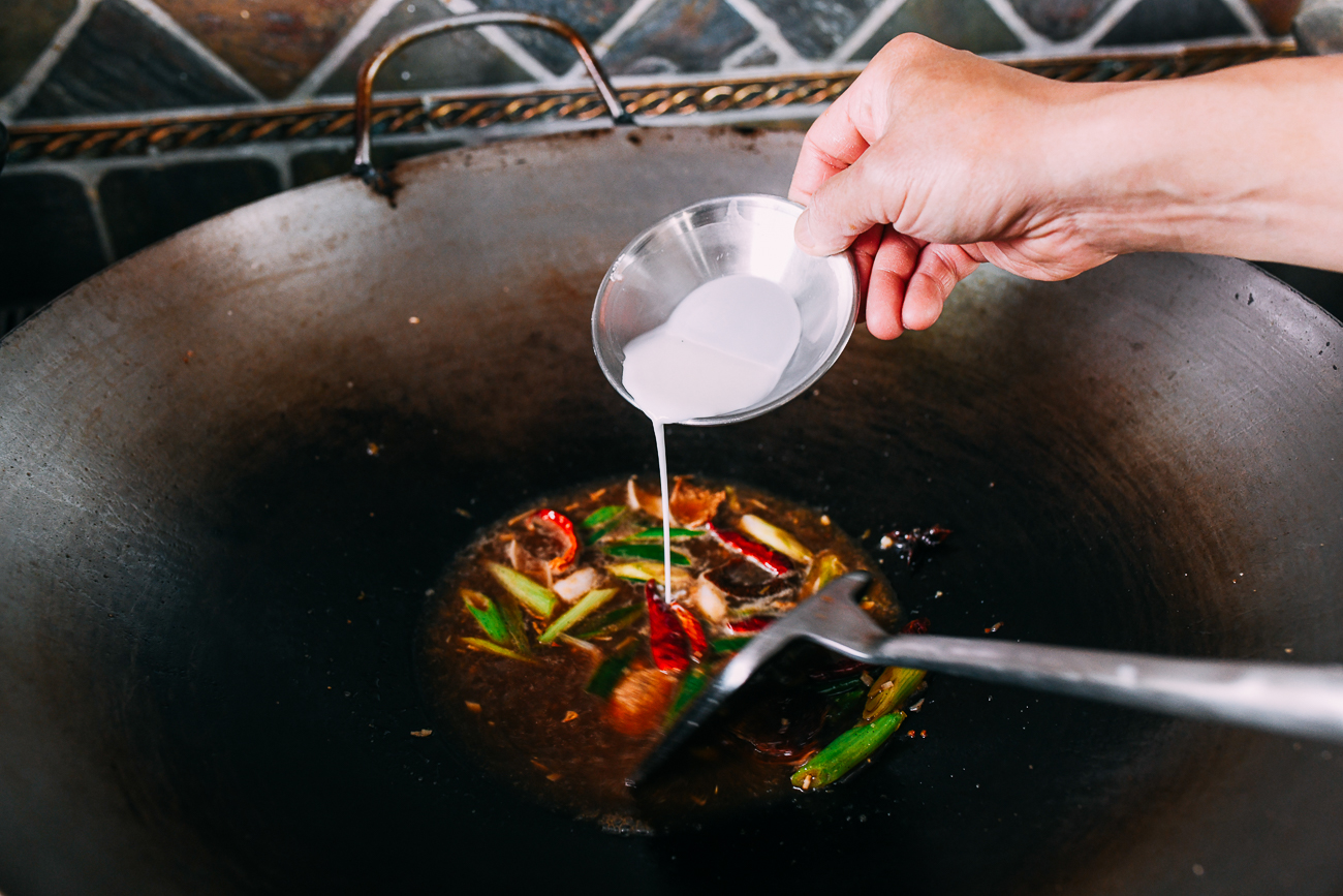 Stirring cornstarch slurry into sauce to thicken it
