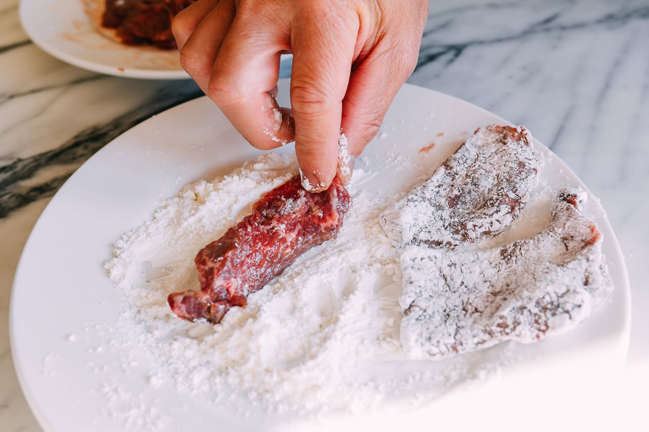 dredging beef slices in cornstarch on a white plate
