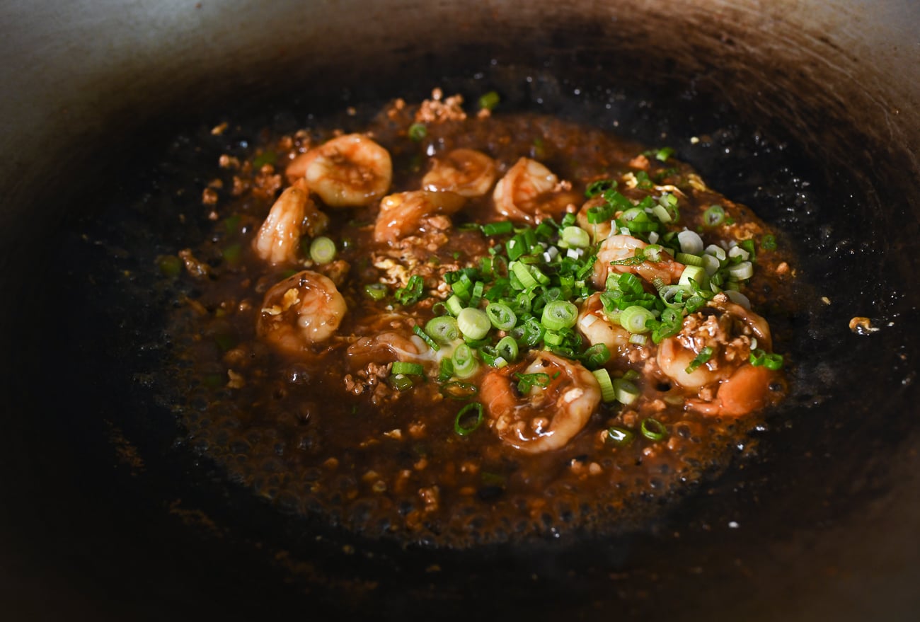 Chopped scallions added to shrimp with black bean sauce in wok