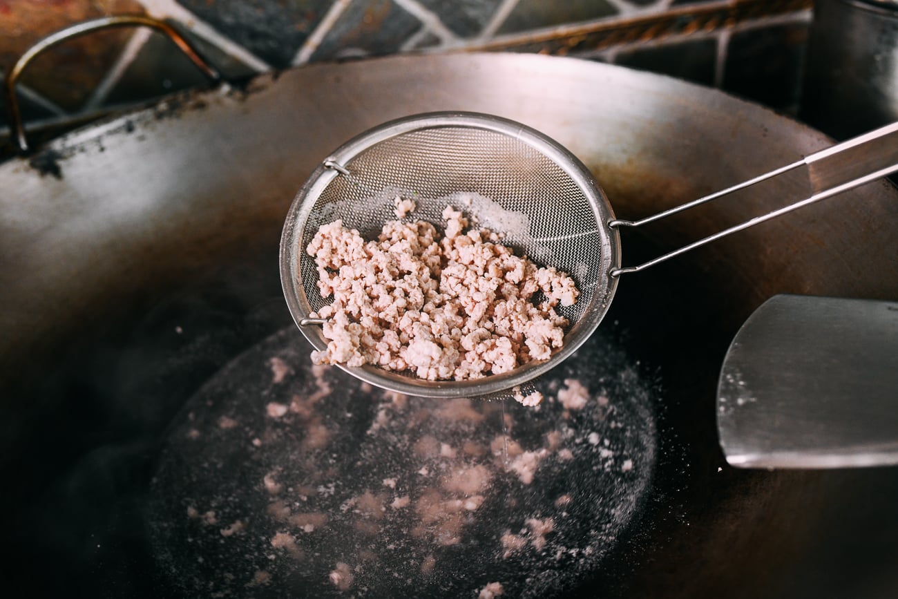 Removing ground pork from wok using a fine mesh strainer