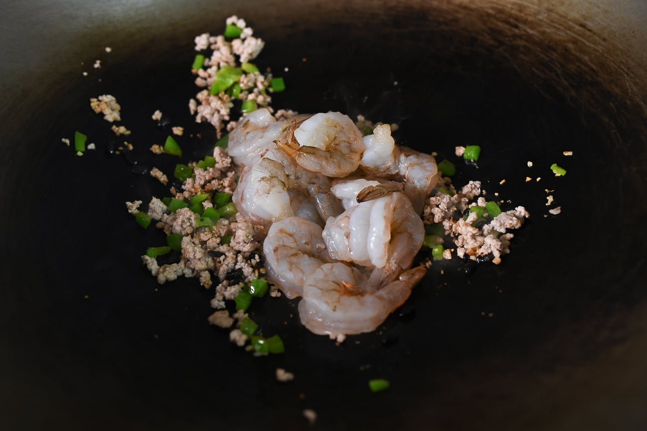 Adding shrimp to wok with pork and peppers