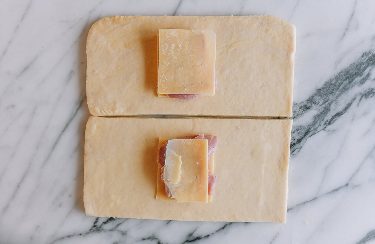 placing ham and cheese on croissant dough