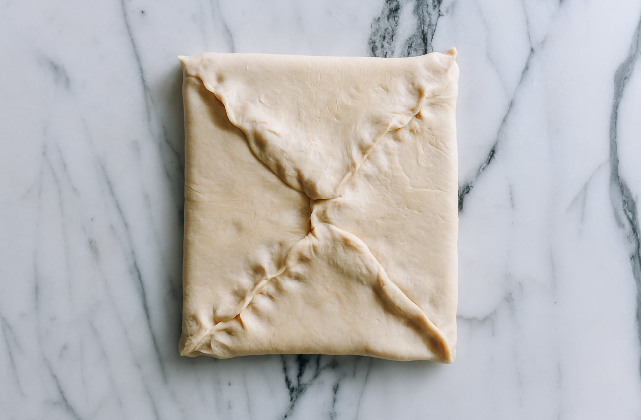 Pinching dough closed around square of butter