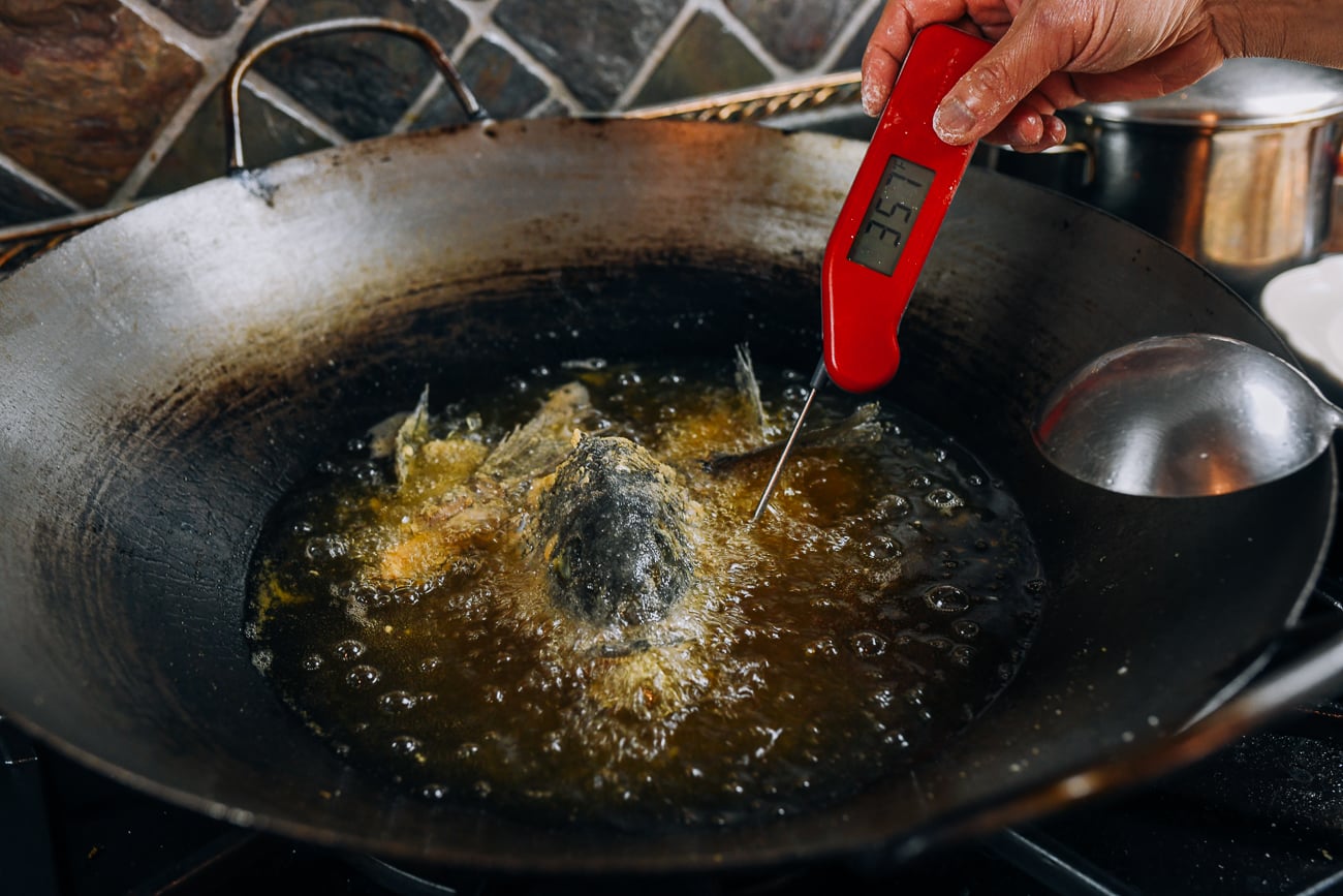 checking temperature of frying oil while frying fish head