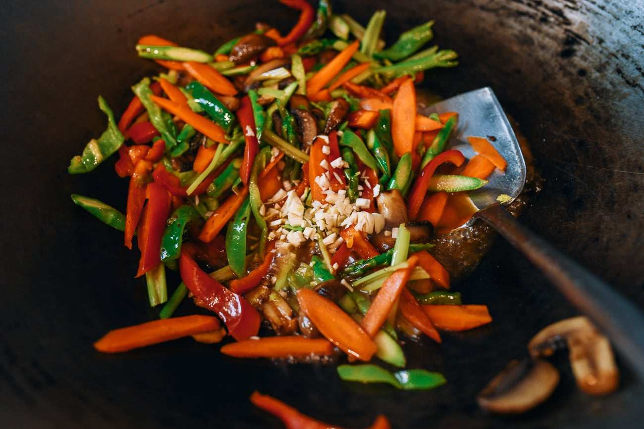 adding garlic and seasoning to mixed vegetable stir-fry