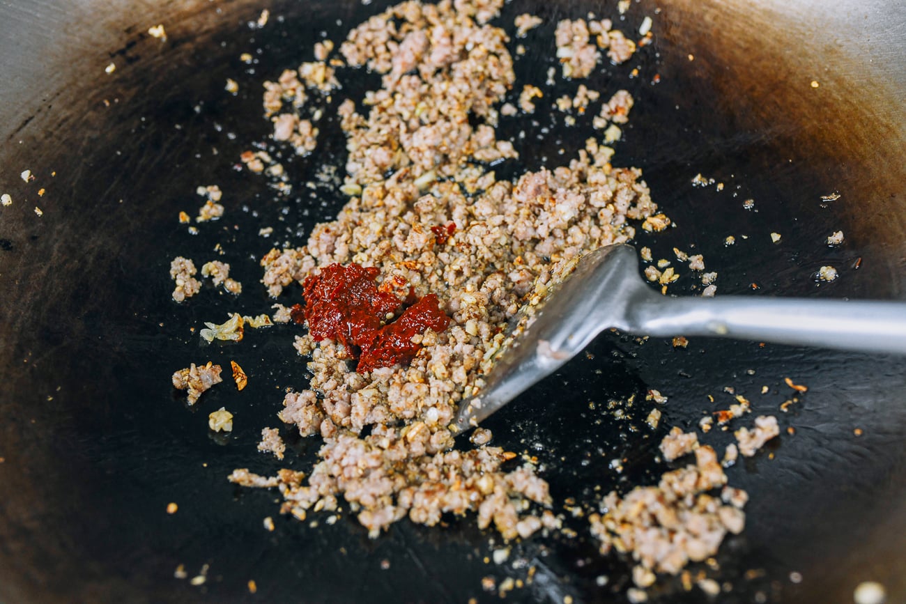 adding spicy bean sauce to ground pork