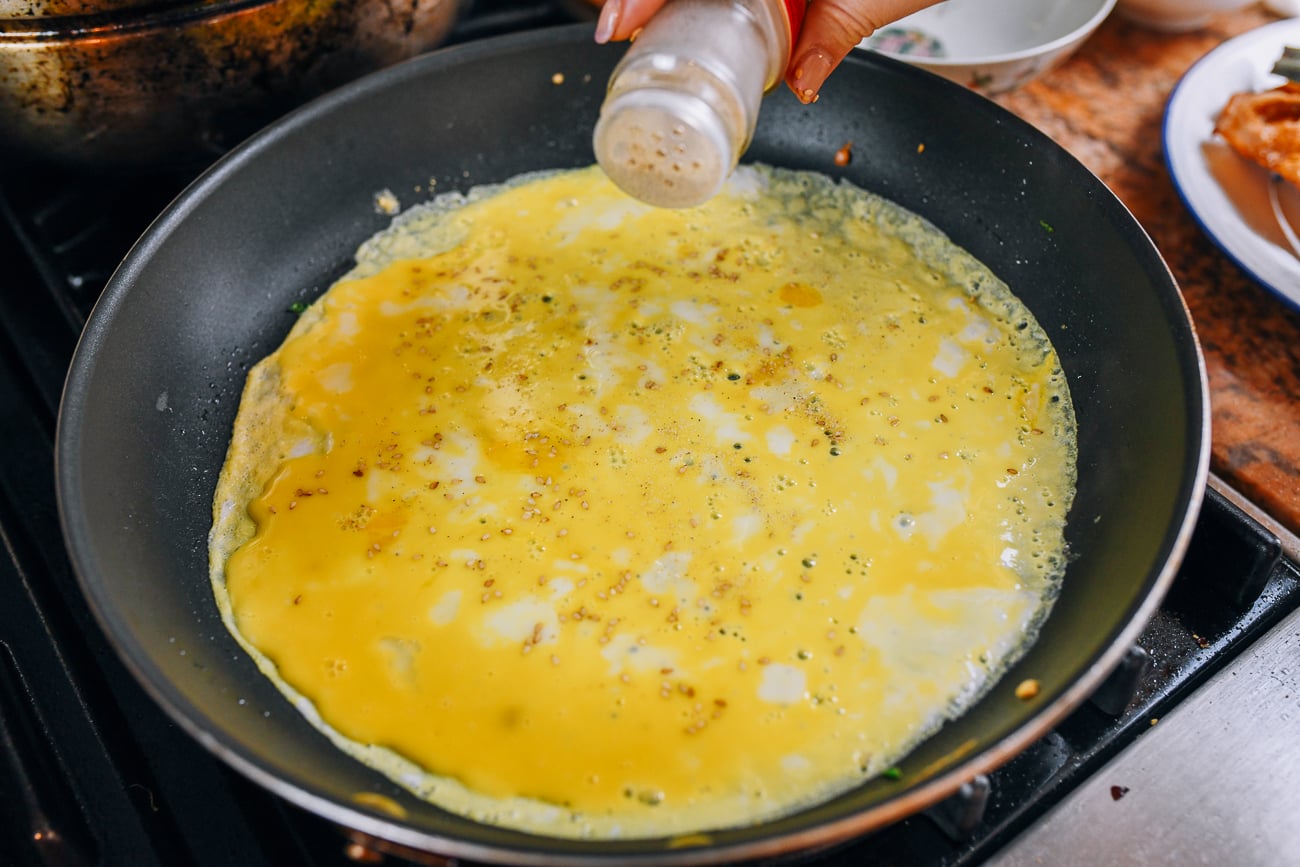 circle of cooked egg in nonstick pan, with sprinkle of sesame seeds