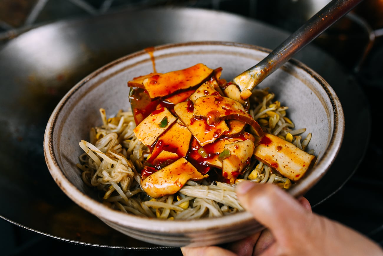 Adding spicy tofu mixture on top of bean sprouts and enoki mushrooms