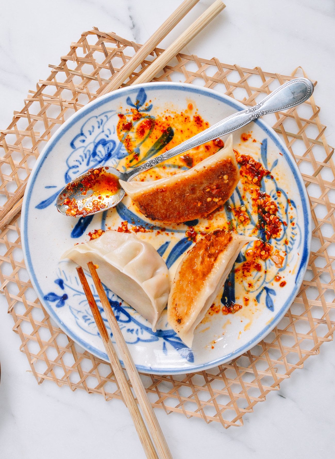 pan-fried dumplings on plate with chopsticks and chili oil