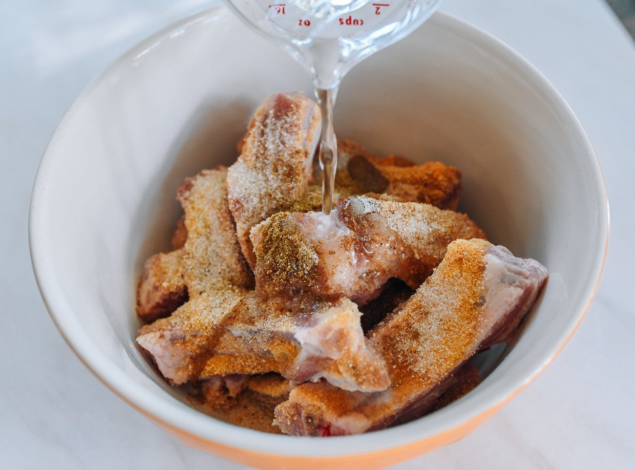 pouring water over ribs and spices in mixing bowl