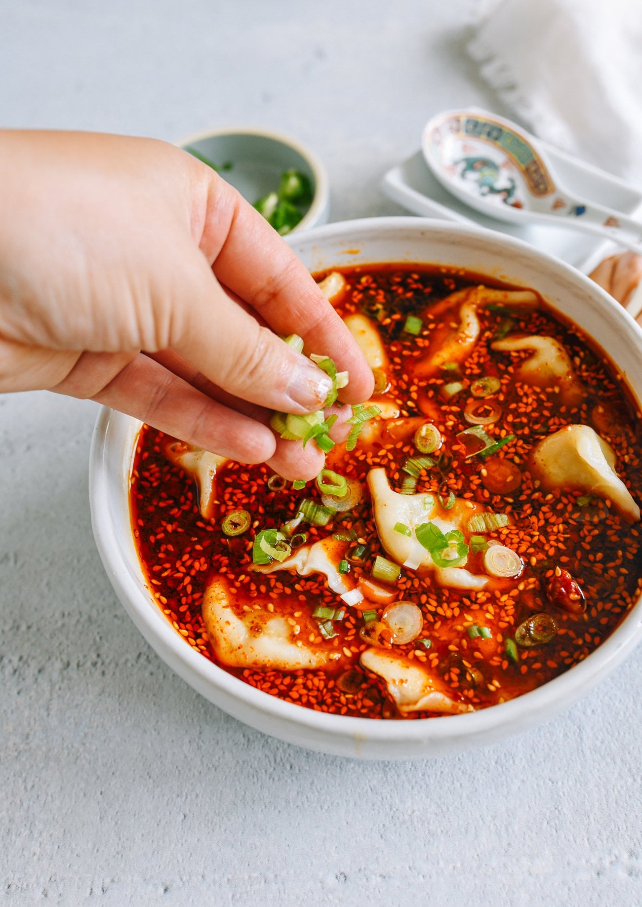 adding scallions to hot and sour dumpling soup