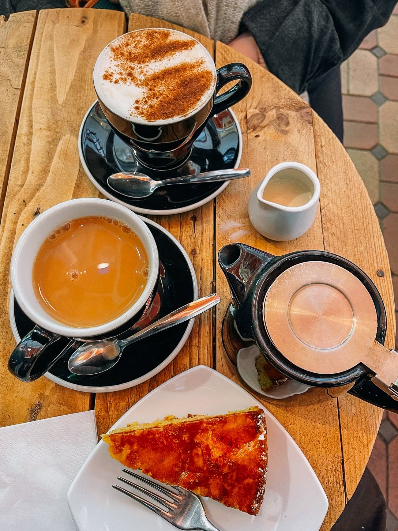 Overhead of a pot of tea, marmalade cake, and a latte covered in cocoa powder