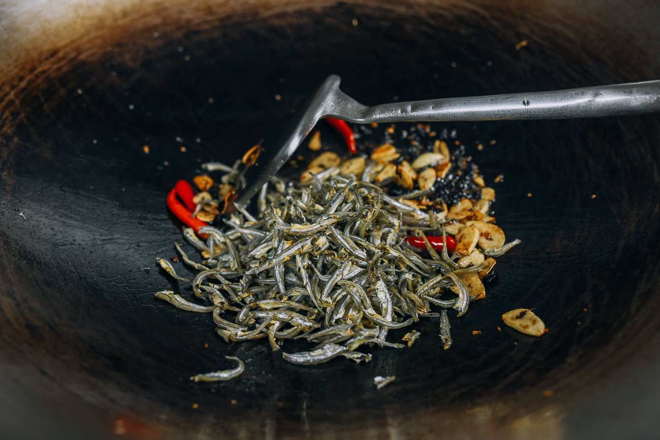 adding dried anchovies to wok