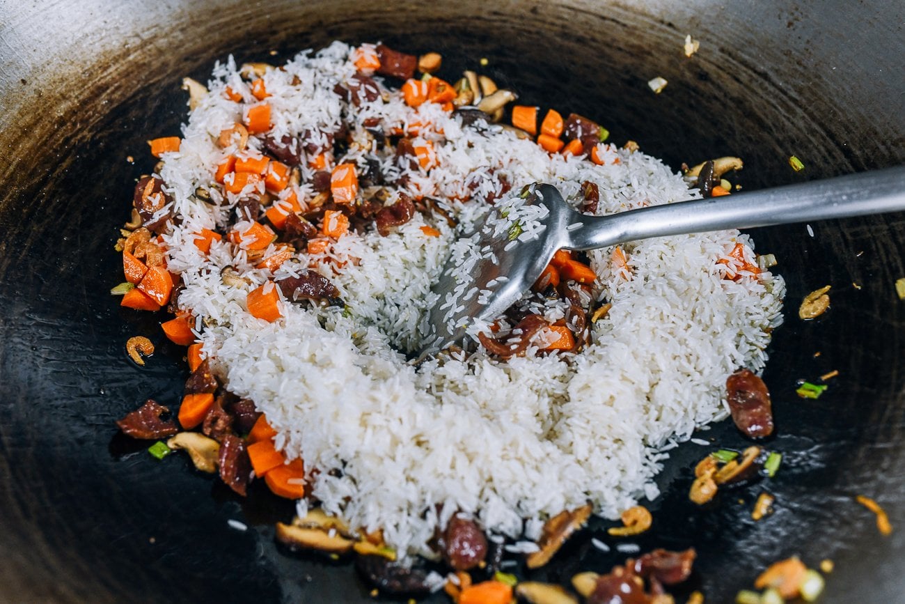 adding raw rice to wok with vegetables and chinese sasuage