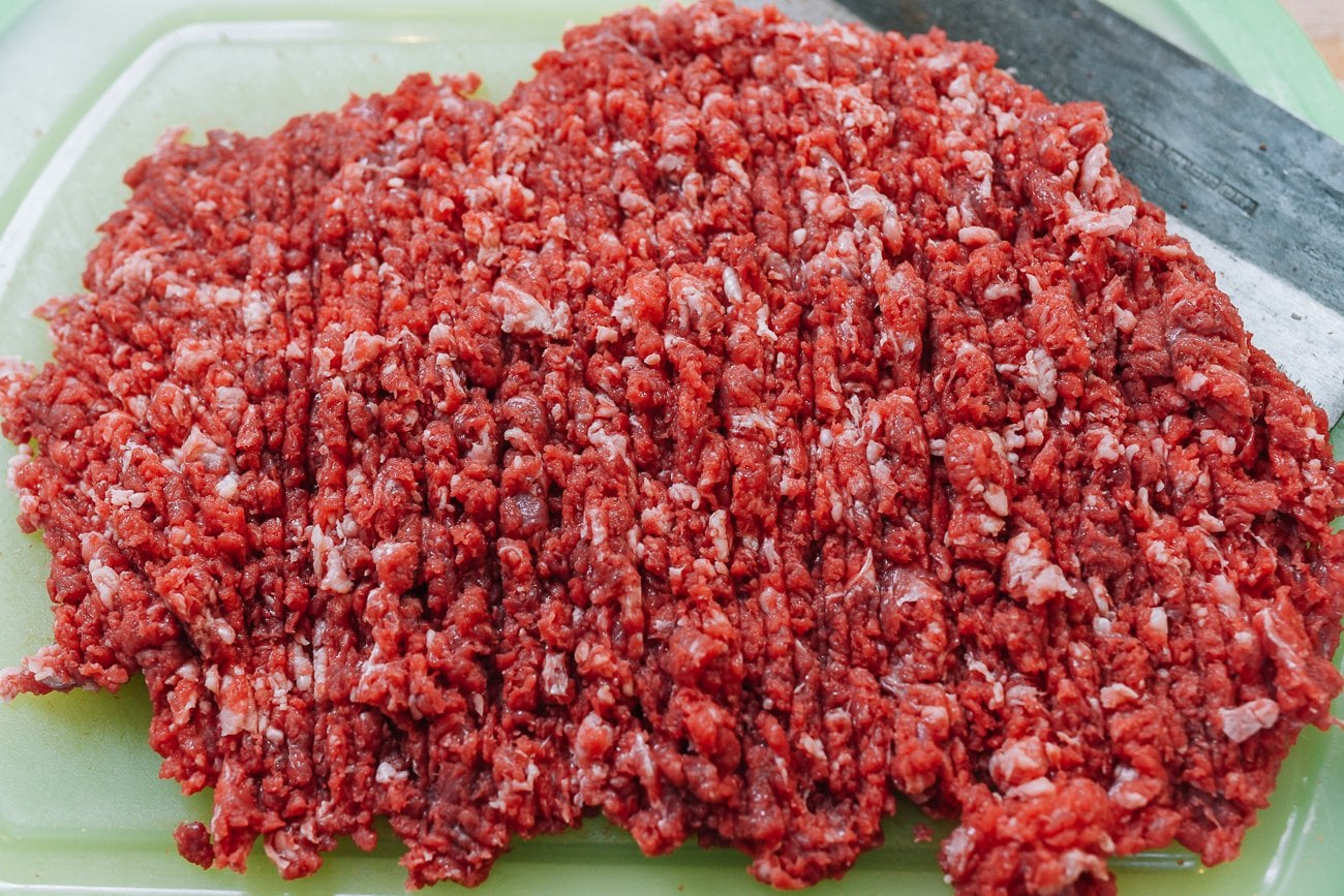 hand chopping beef on cutting board with cleaver