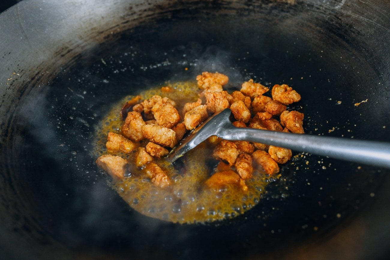 tossing fried chicken pieces into sauce