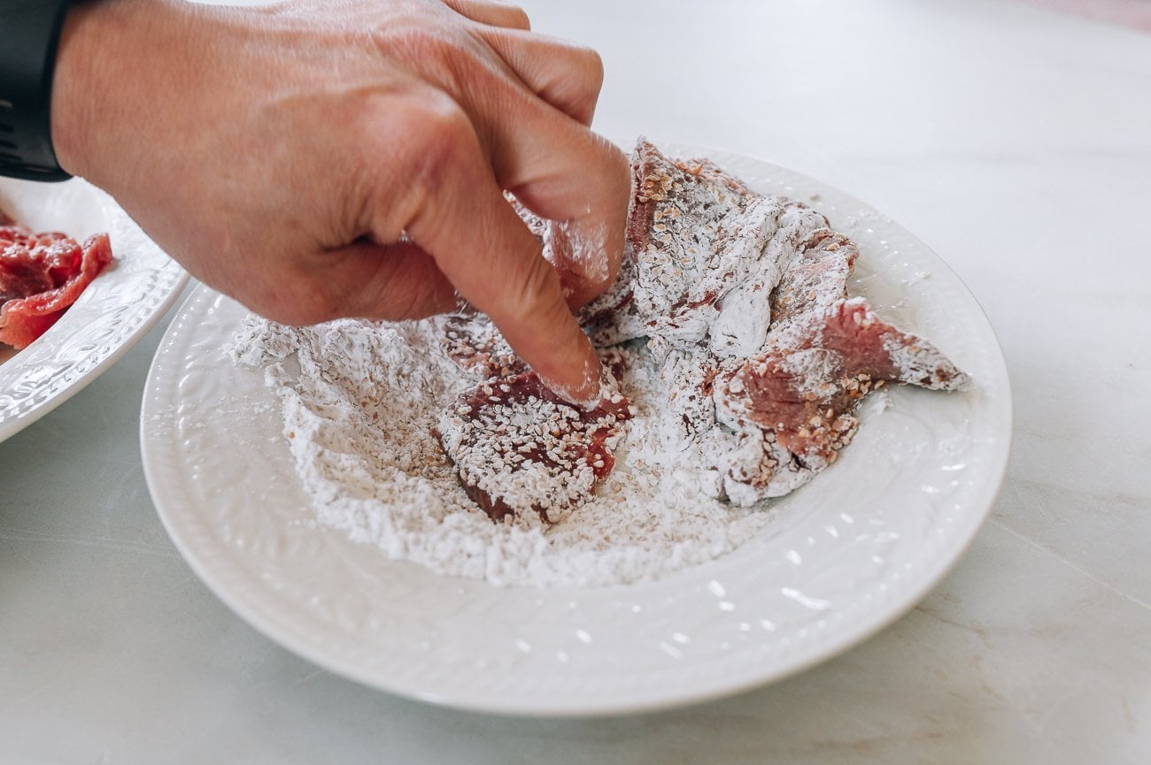 dredging beef slices in cornstarch and sesame seeds