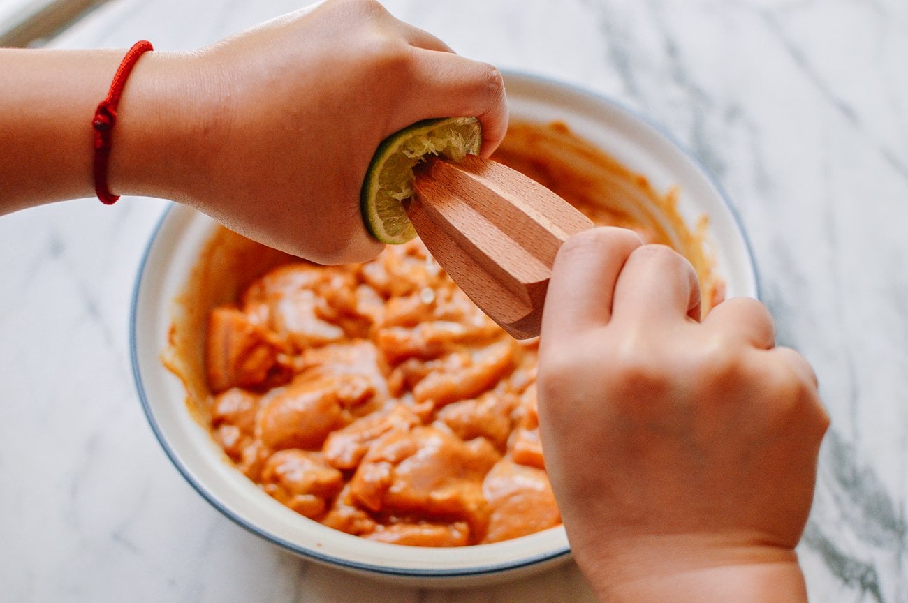 adding lime juice to marinating chicken in bowl
