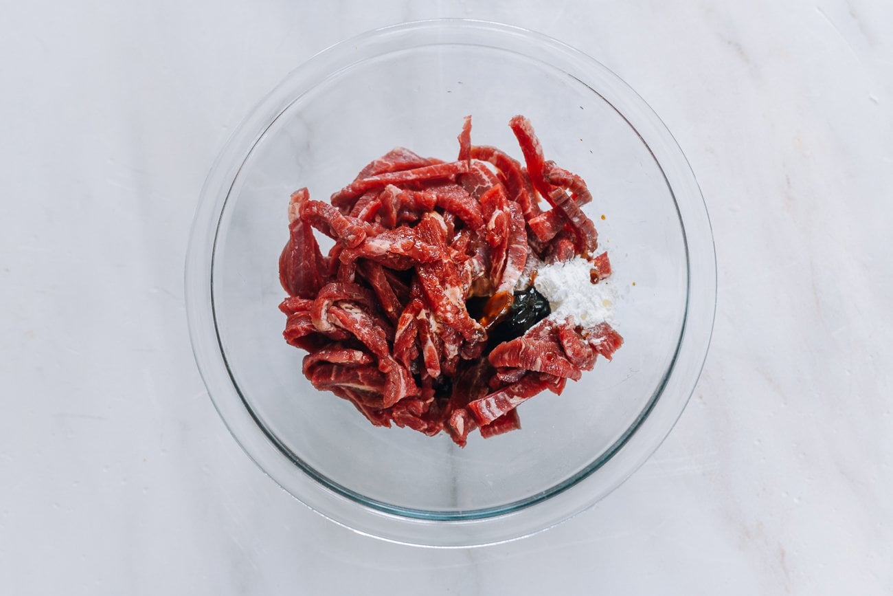 adding marinade ingredients to beef strips