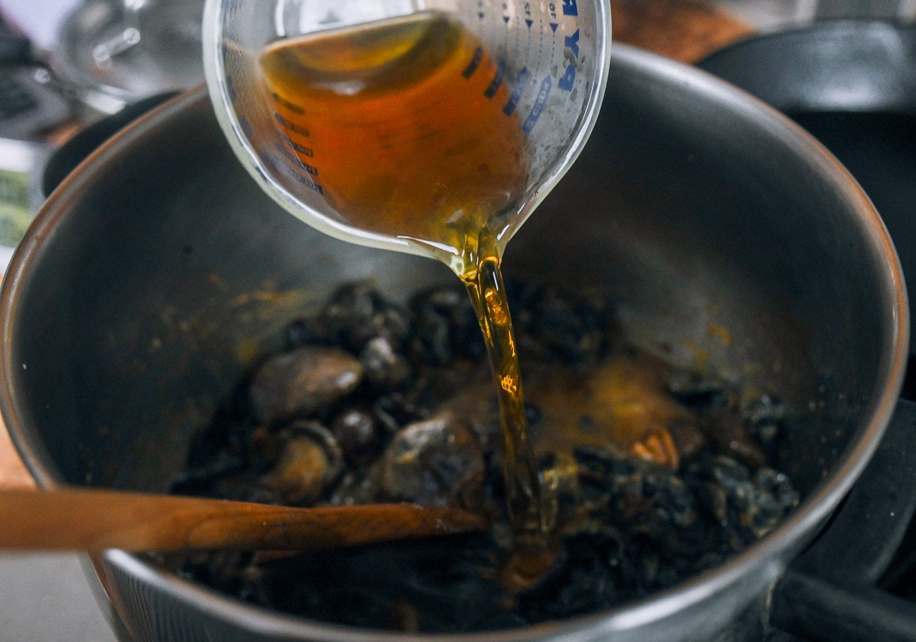 adding mushroom soaking liquid to pot with reconstituted mushrooms