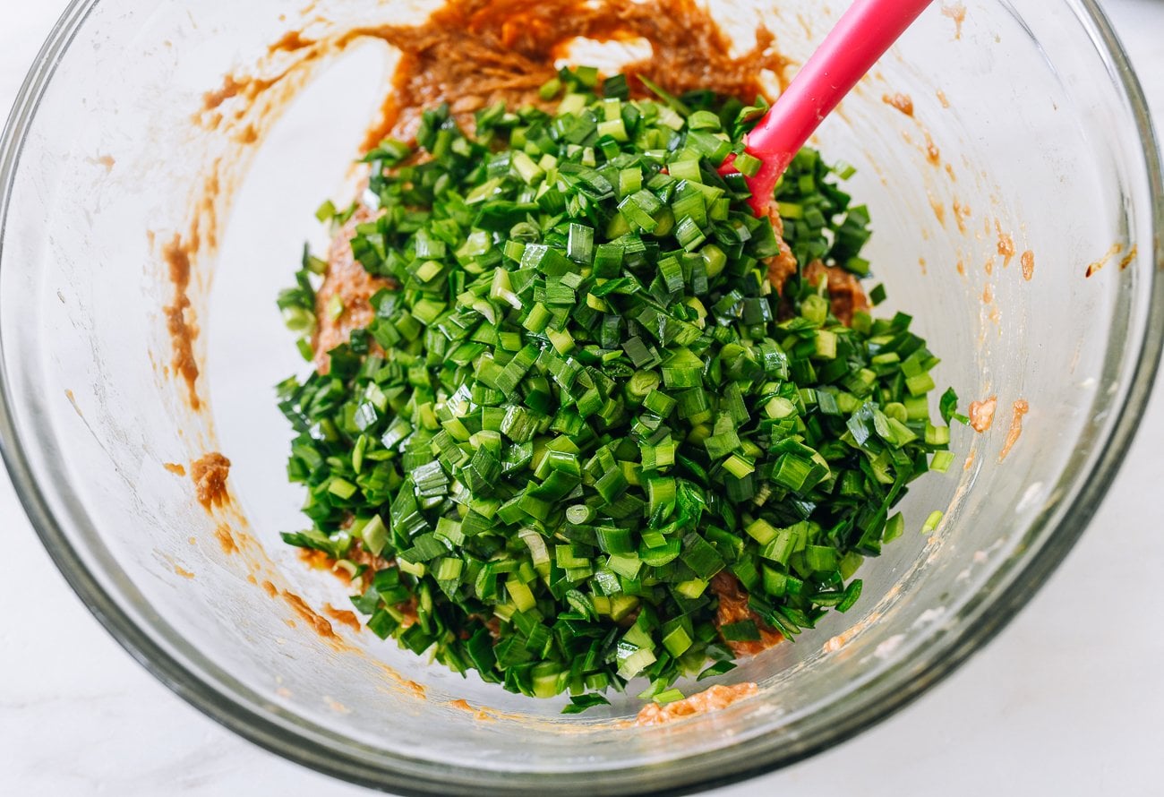 garlic chives added to ground pork in glass mixing bowl