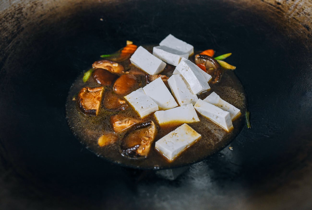 tofu added to vegetables and sauce in wok
