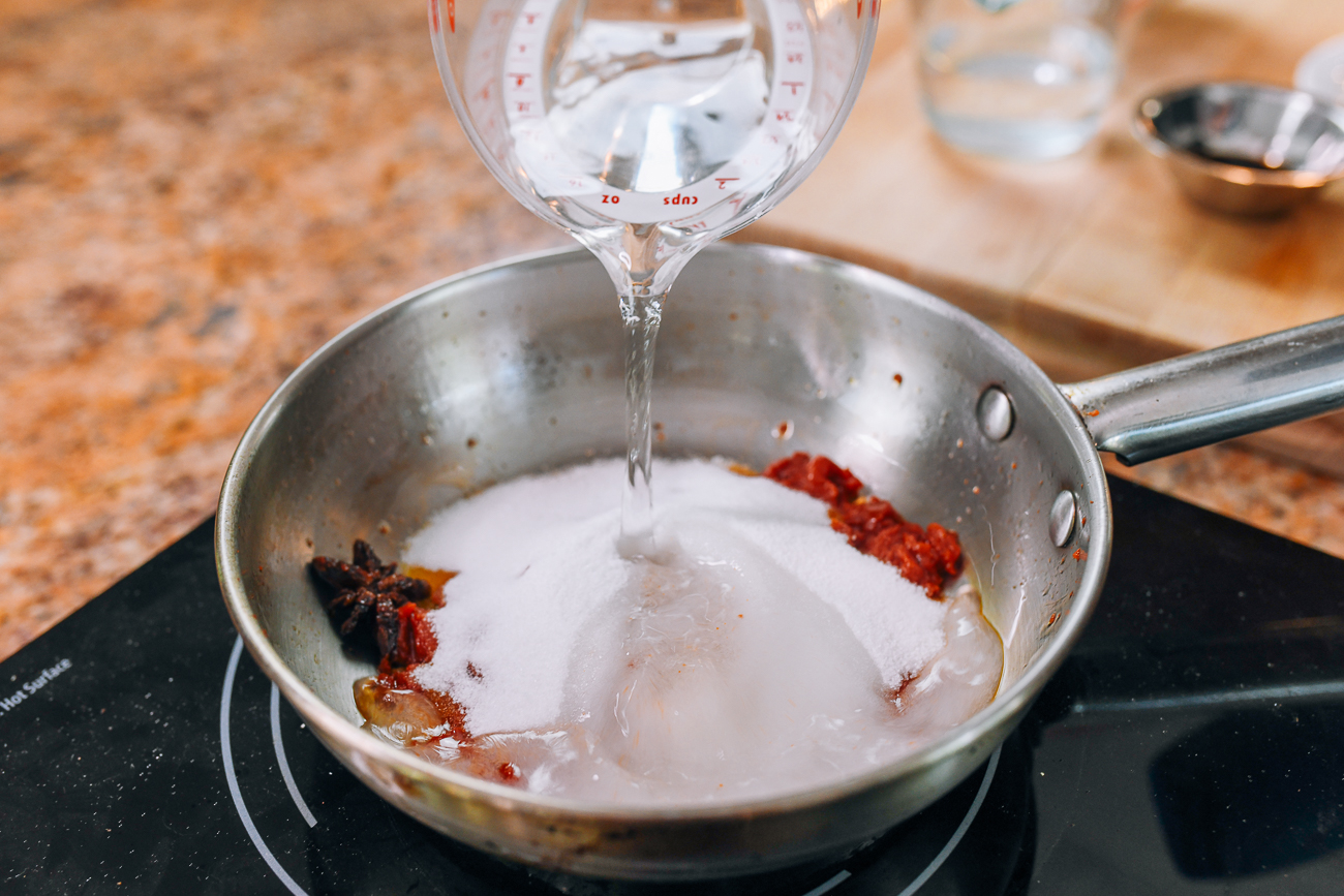 adding sugar and water to tomato paste to make sweet and sour sauce