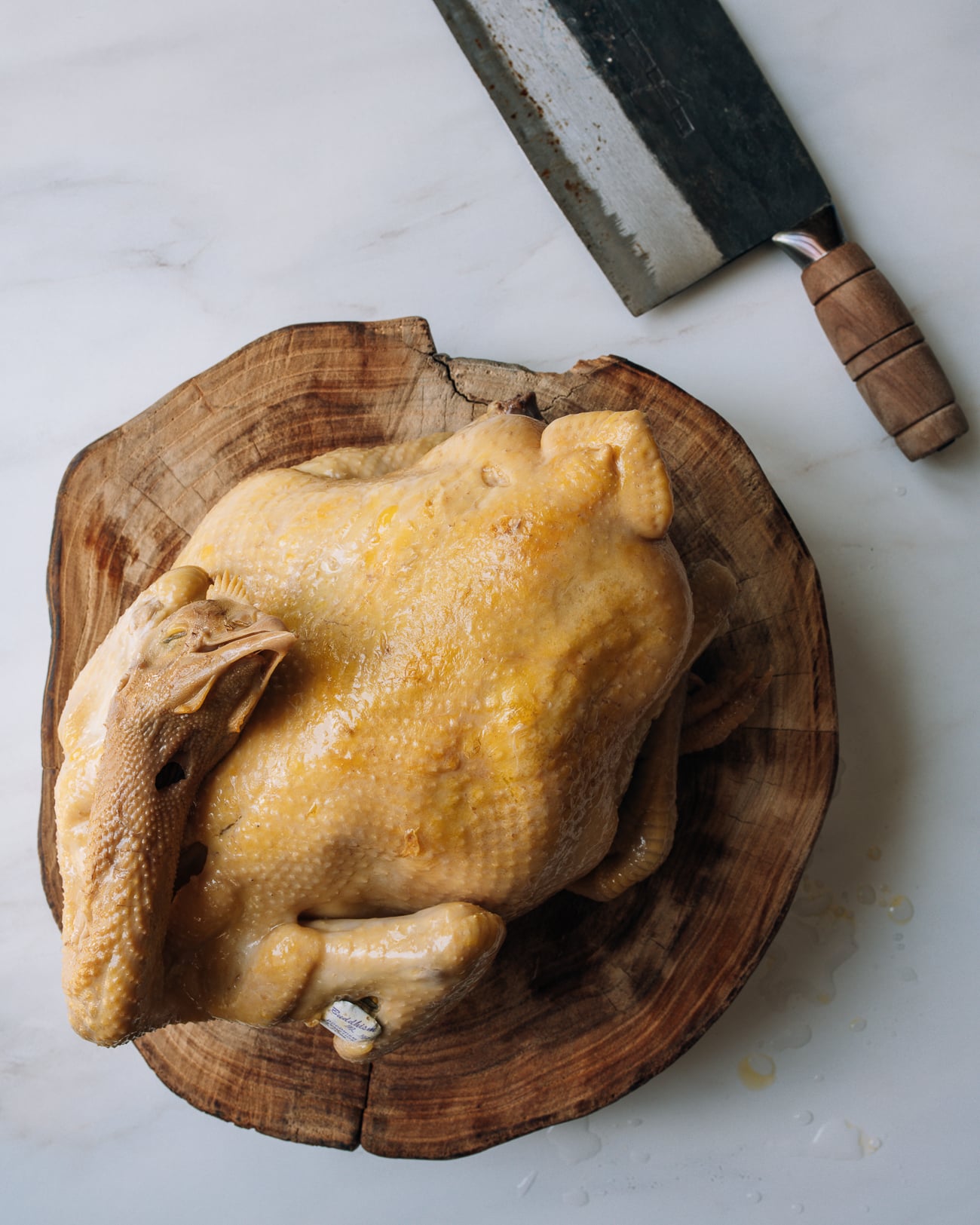 whole Chinese poached chicken on cutting board with cleaver