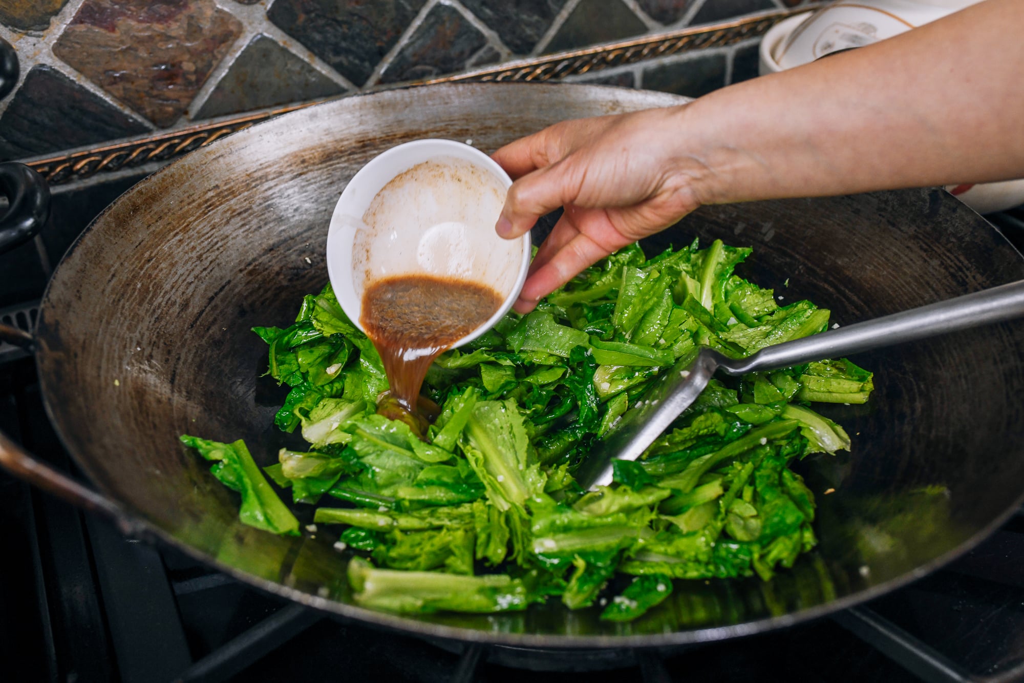 adding sauce to AA choy in wok