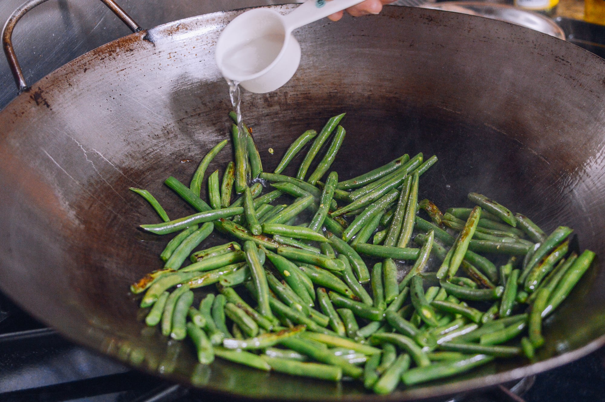 adding water to string beans in wok