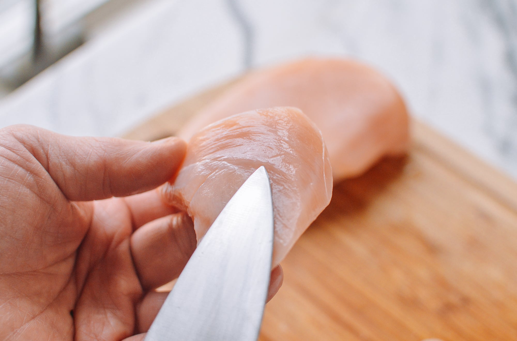 holding piece of chicken breast and pointing at the grain of the meat with a knife