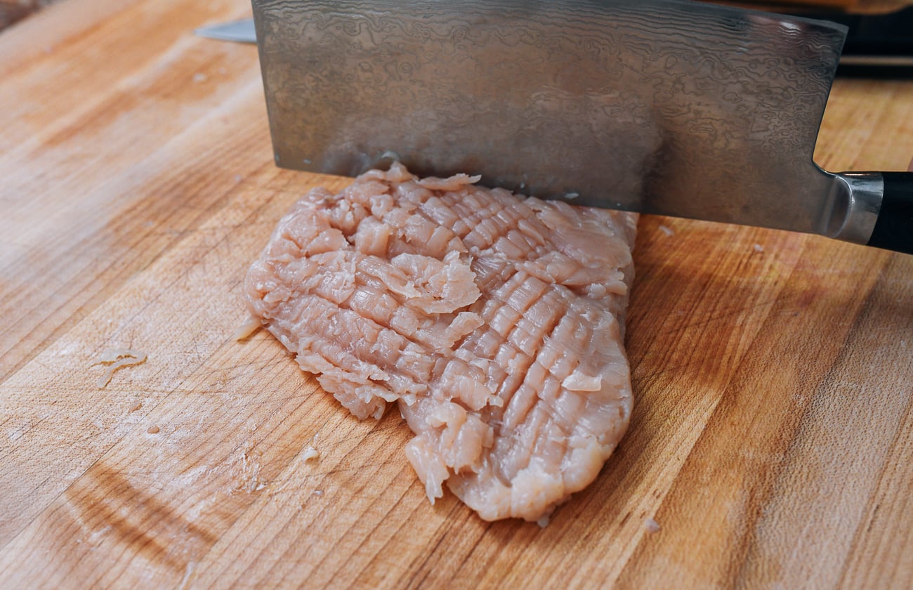 pounding chicken breast with back of chinese cleaver in a crosshatch pattern