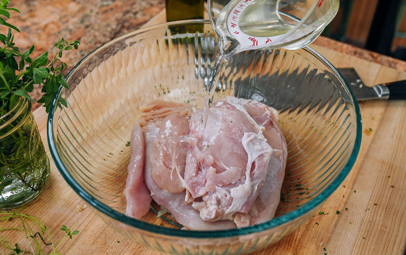 pouring water over boneless chicken breasts in bowl