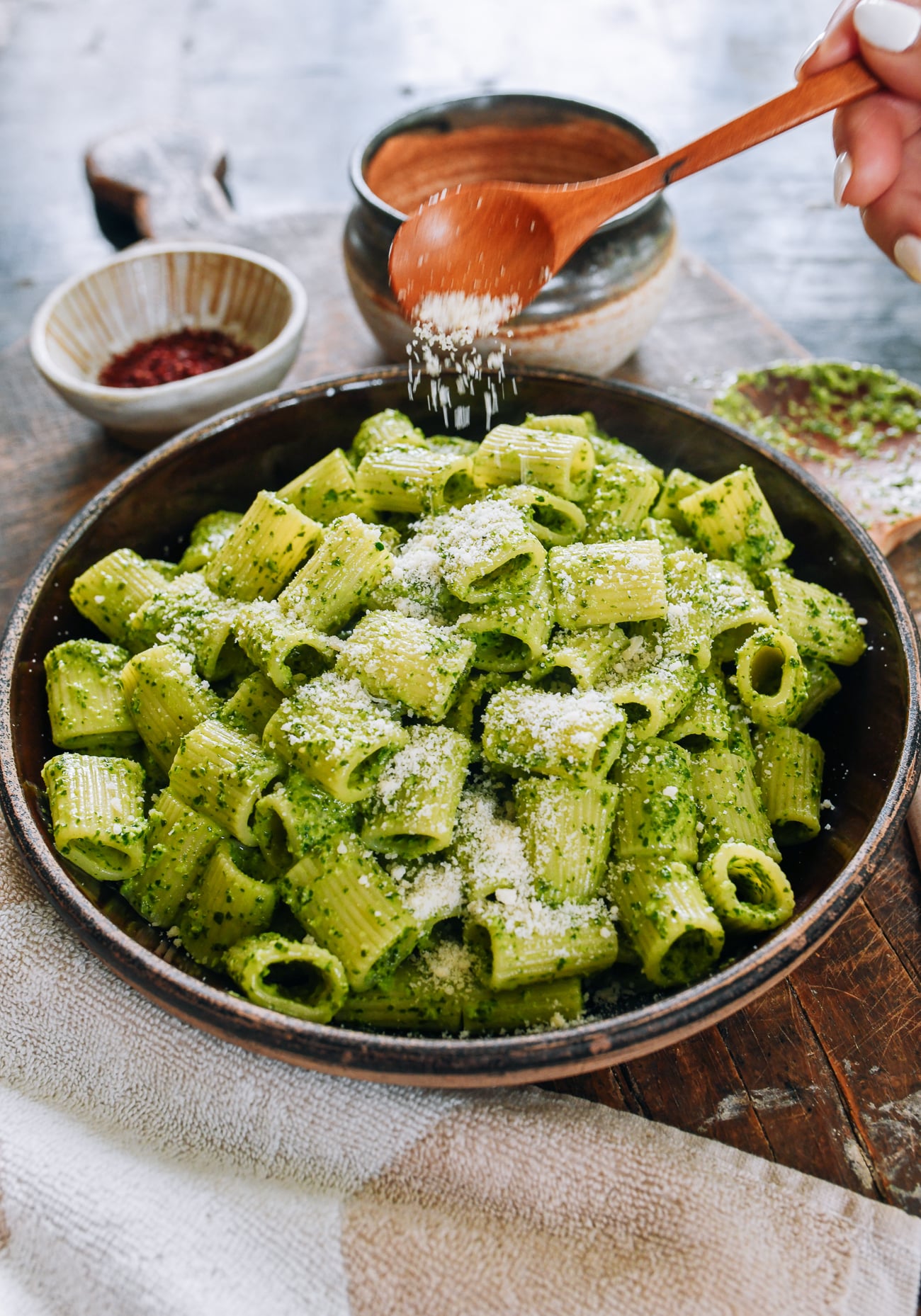 sprinkling parmesan cheese on pesto pasta