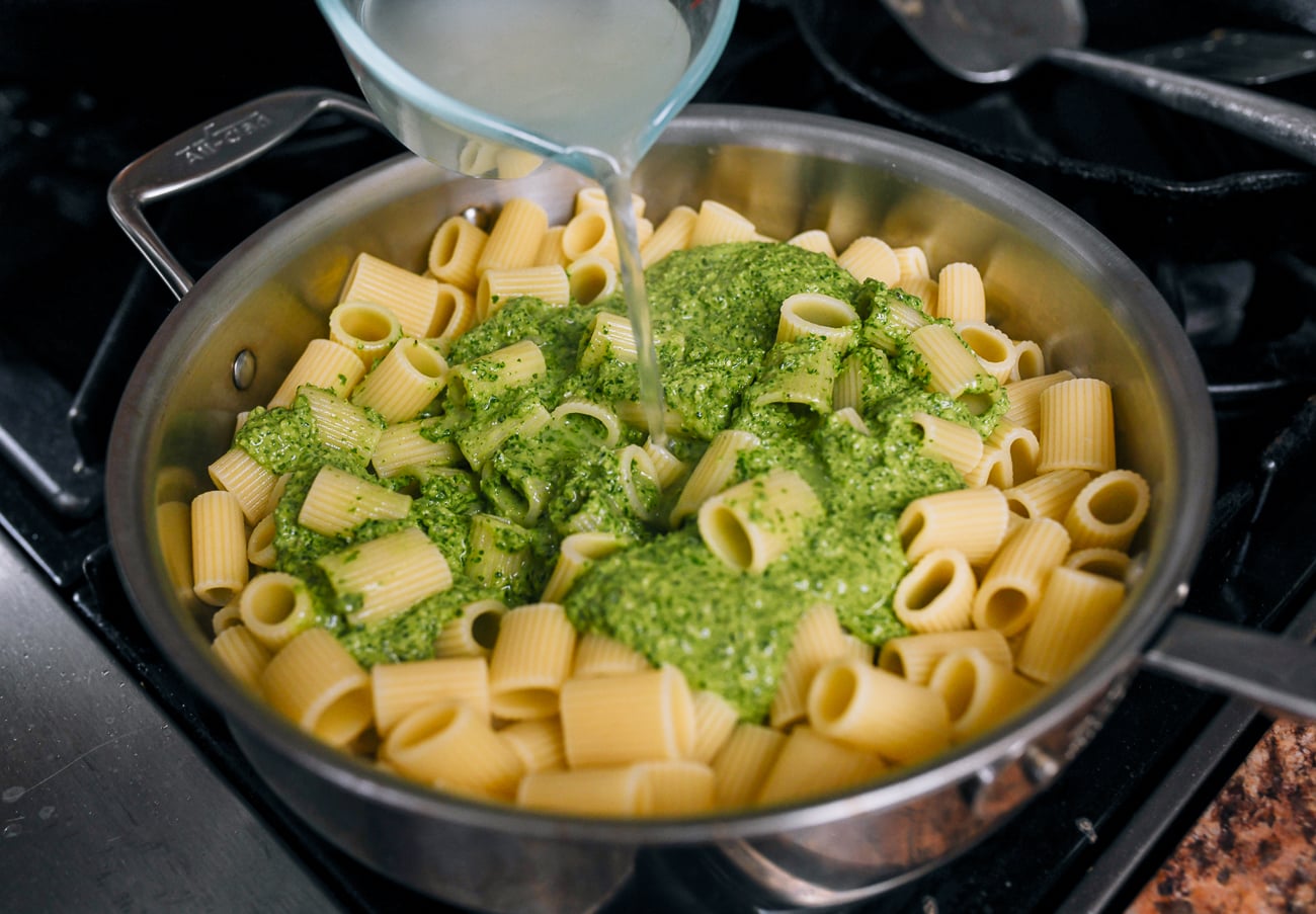 adding pasta water to rigatoni with pesto