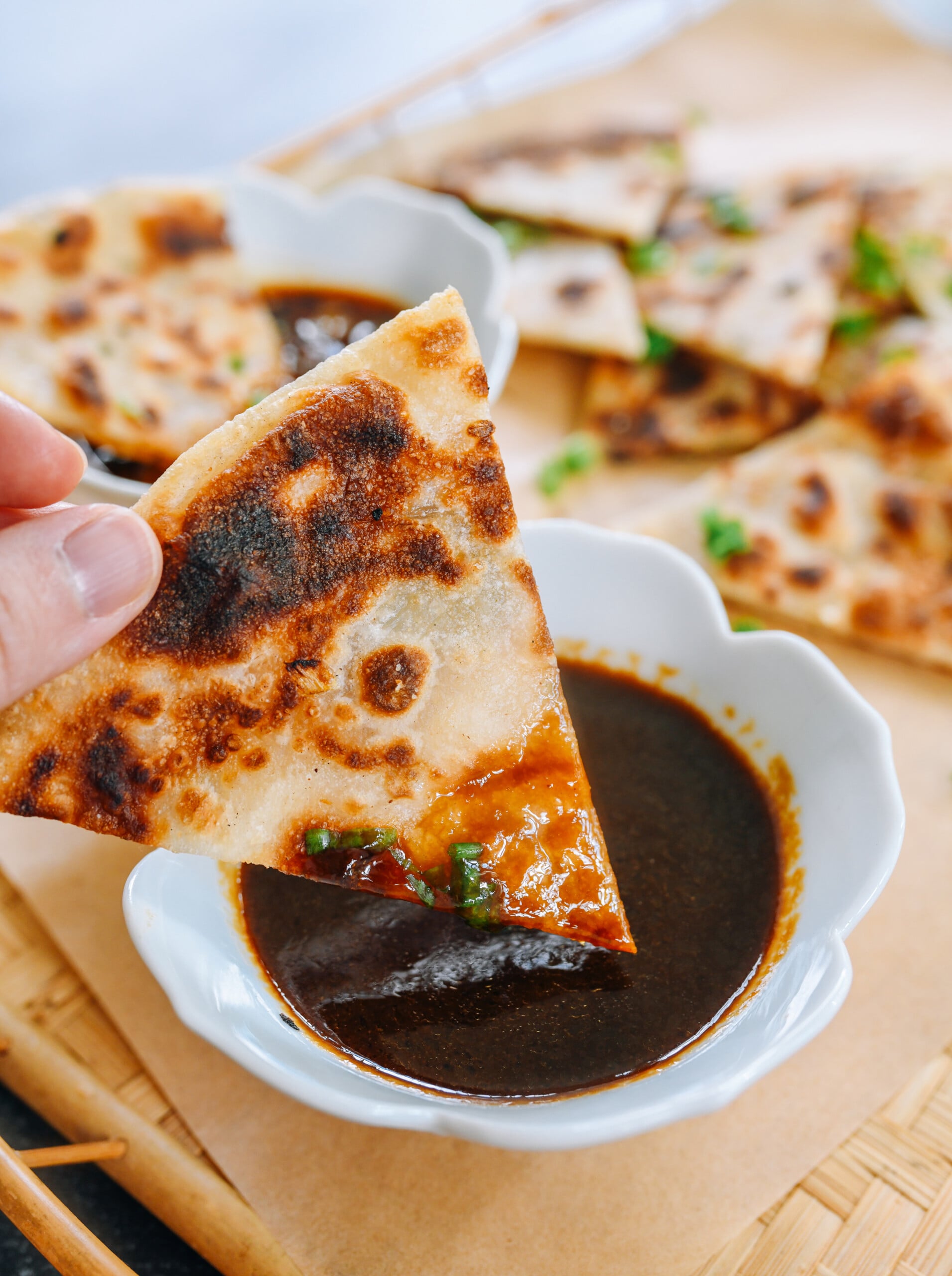 dipping scallion pancake wedge into hoisin based dipping sauce