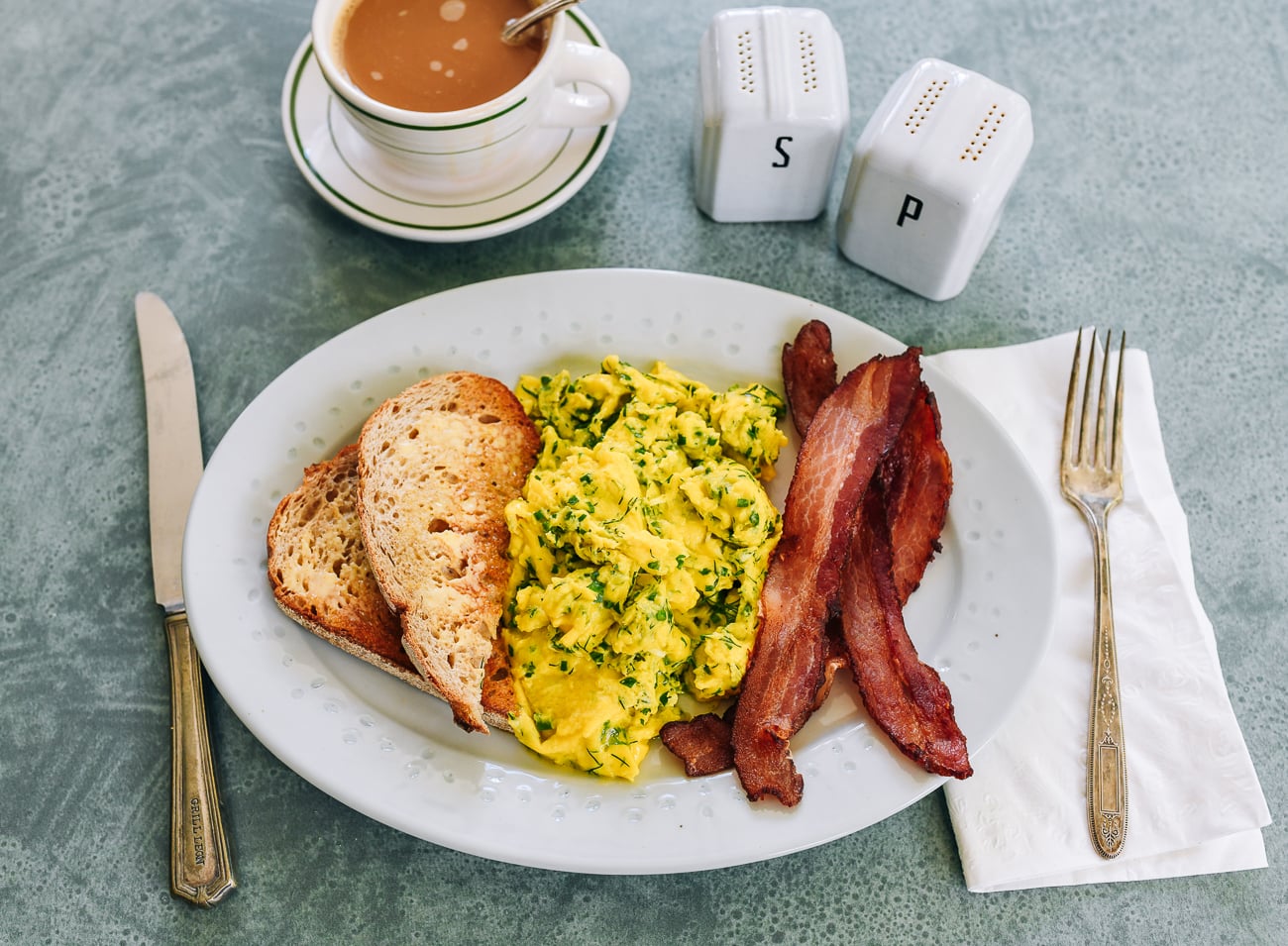 herby scrambled eggs with toast and bacon and coffee