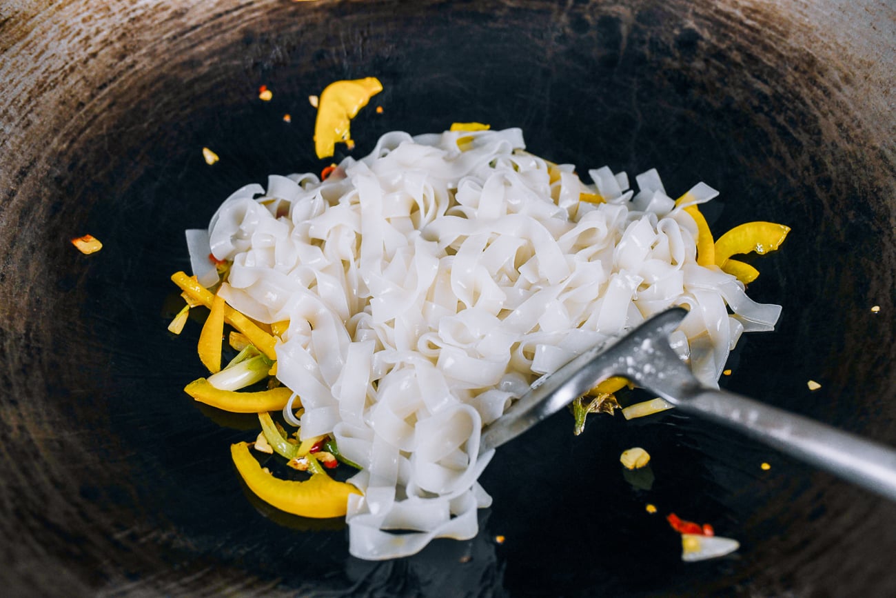 rice noodles added to peppers in wok