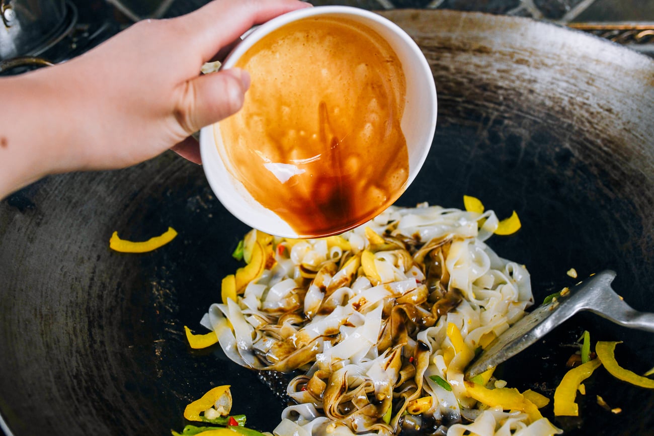 adding sauce mixture to rice noodles in wok